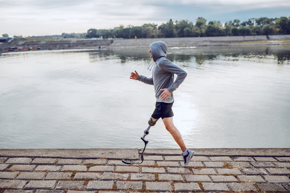 운동복을 입은 건강한 백인 장애인 스포츠맨과 부두에서 달리는 인공 다리의 측면 보기.