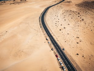 Aerial view of black asphalt road in the middle of the beach - desert around and concept of travel and vacation.   tropical scenic place - transport and parked cars in  wild landscape