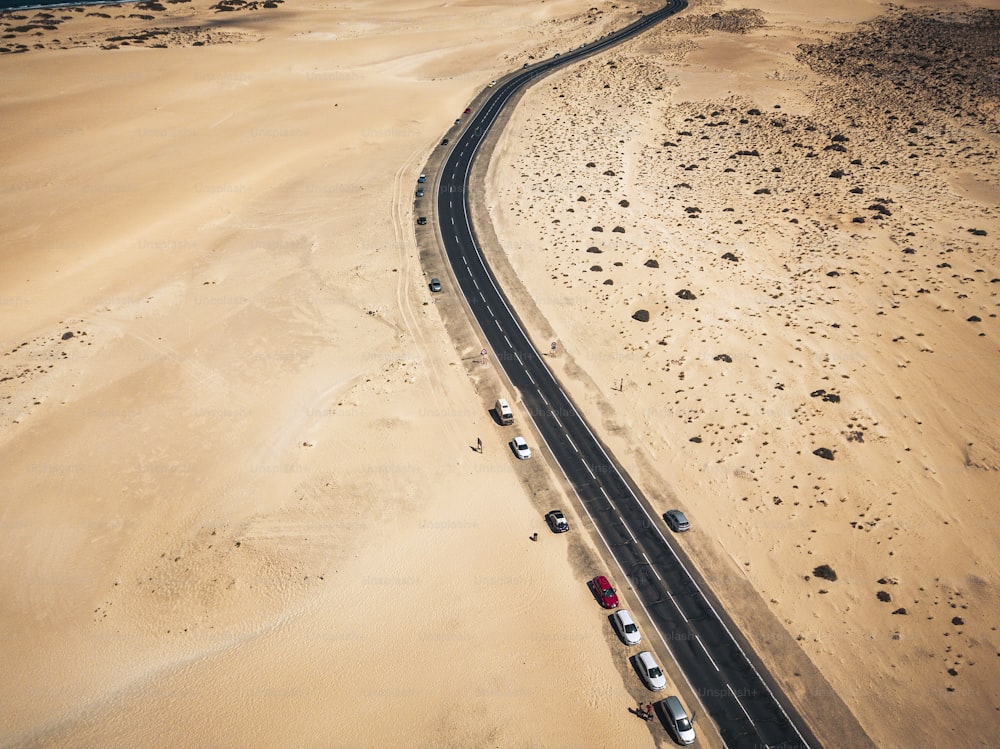 Aerial view of black asphalt road in the middle of the beach - desert around and concept of travel and vacation.   tropical scenic place - transport and parked cars in  wild landscape