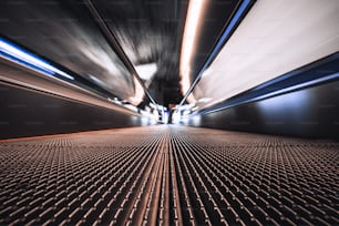 Long exposure shooting from the bottom of a moving walkway in an airport terminal; travelator through contemporary departure area of railway station depot with stretching to the vanishing point
