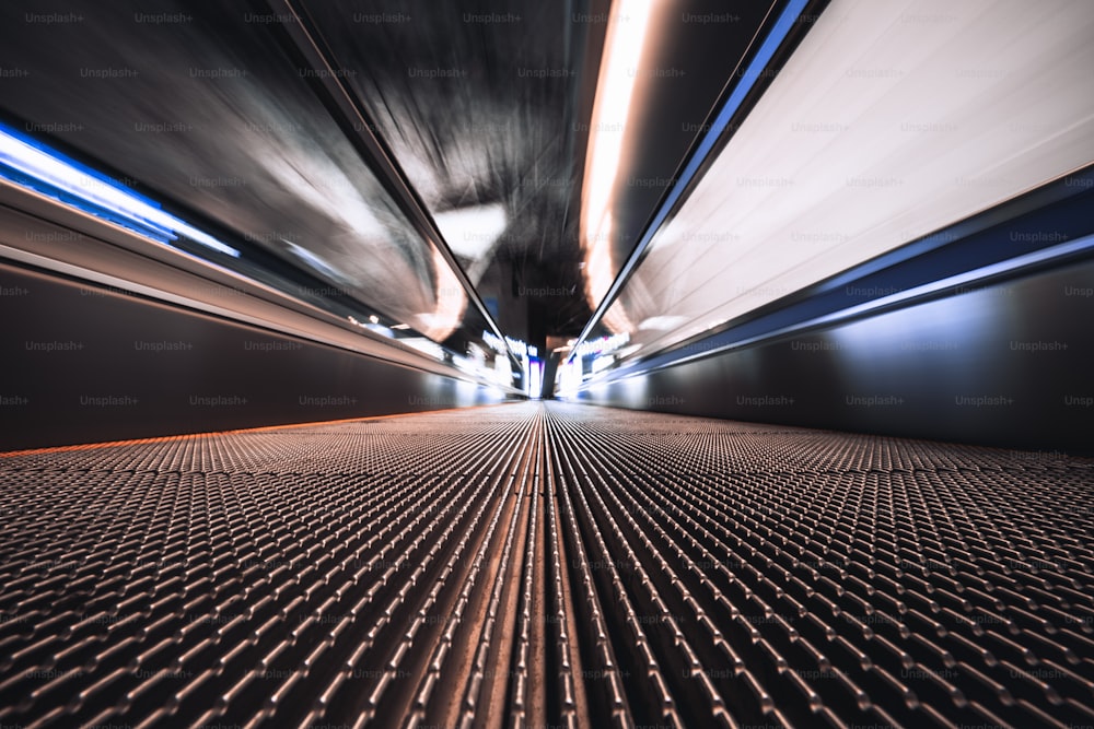 Long exposure shooting from the bottom of a moving walkway in an airport terminal; travelator through contemporary departure area of railway station depot with stretching to the vanishing point