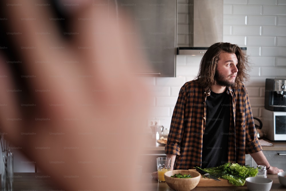 Close up portrait of two men in the kitchen at home, showing complication of relationship, one man is cooking, another is talking on the phone