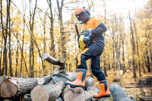 Bûcheron professionnel en vêtements de travail protecteurs travaillant avec une tronçonneuse dans la forêt. Un bûcheron fait une exploitation forestière à l’extérieur