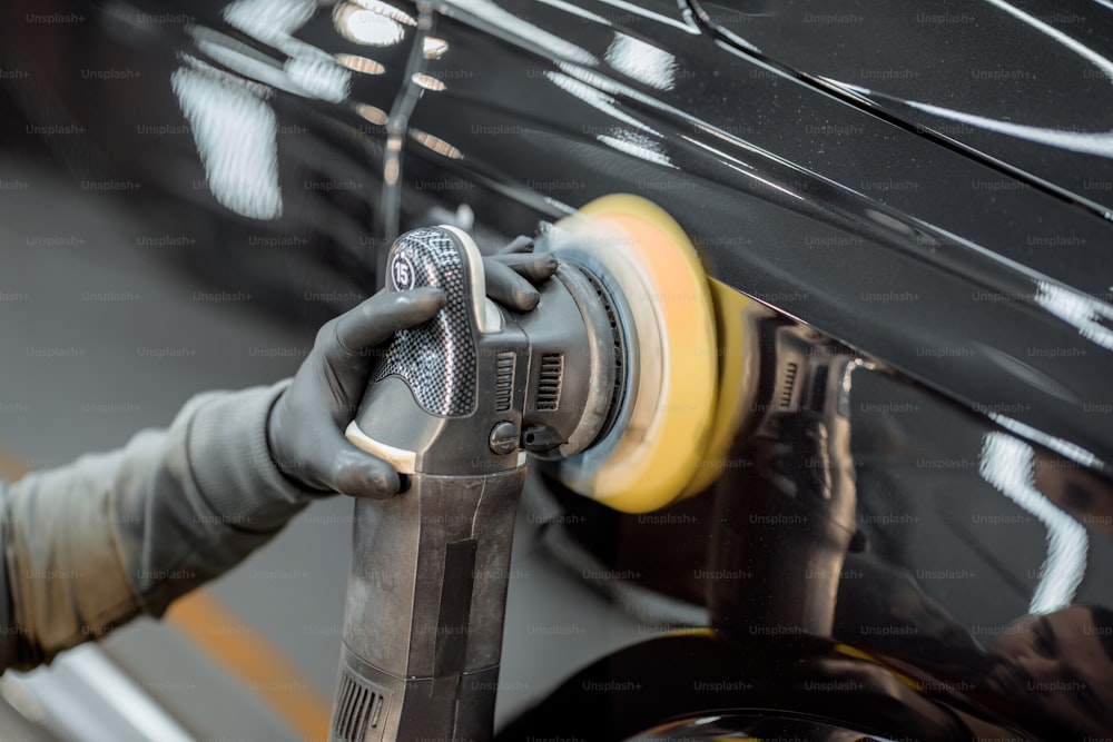 Car service worker polishing vehicle body with special wax from scratches, close-up. Professional car detailing and maintenance concept