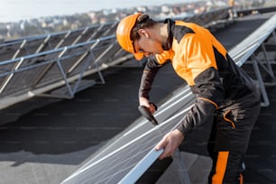 Trabajador bien equipado con ropa protectora naranja instalando o reemplazando paneles solares en una planta fotovoltaica en la azotea. Concepto de mantenimiento e instalación de estaciones solares