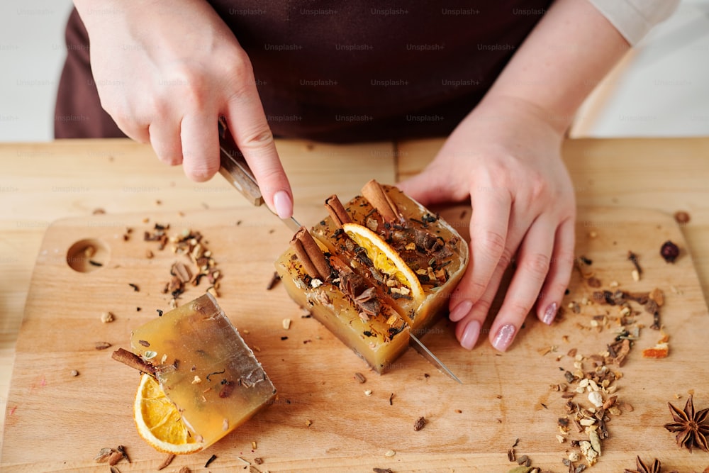 Hands of girl with knife cutting handmade soap bar with aromatic cinnamon, star anise and orange slices