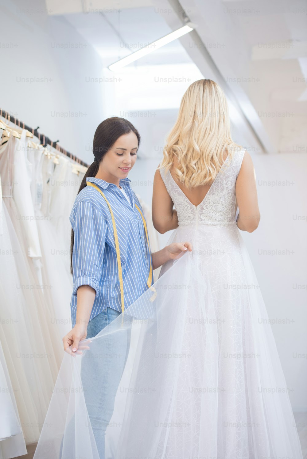Conteúdo jovem costureira ajustando bainha de vestido de noiva durante o vestido de encaixe no estúdio