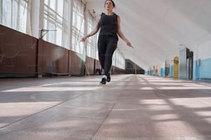 Vista de ángulo bajo de una atleta femenina tatuada en ropa deportiva negra saltando sobre la cuerda mientras hace ejercicio en un gimnasio espacioso