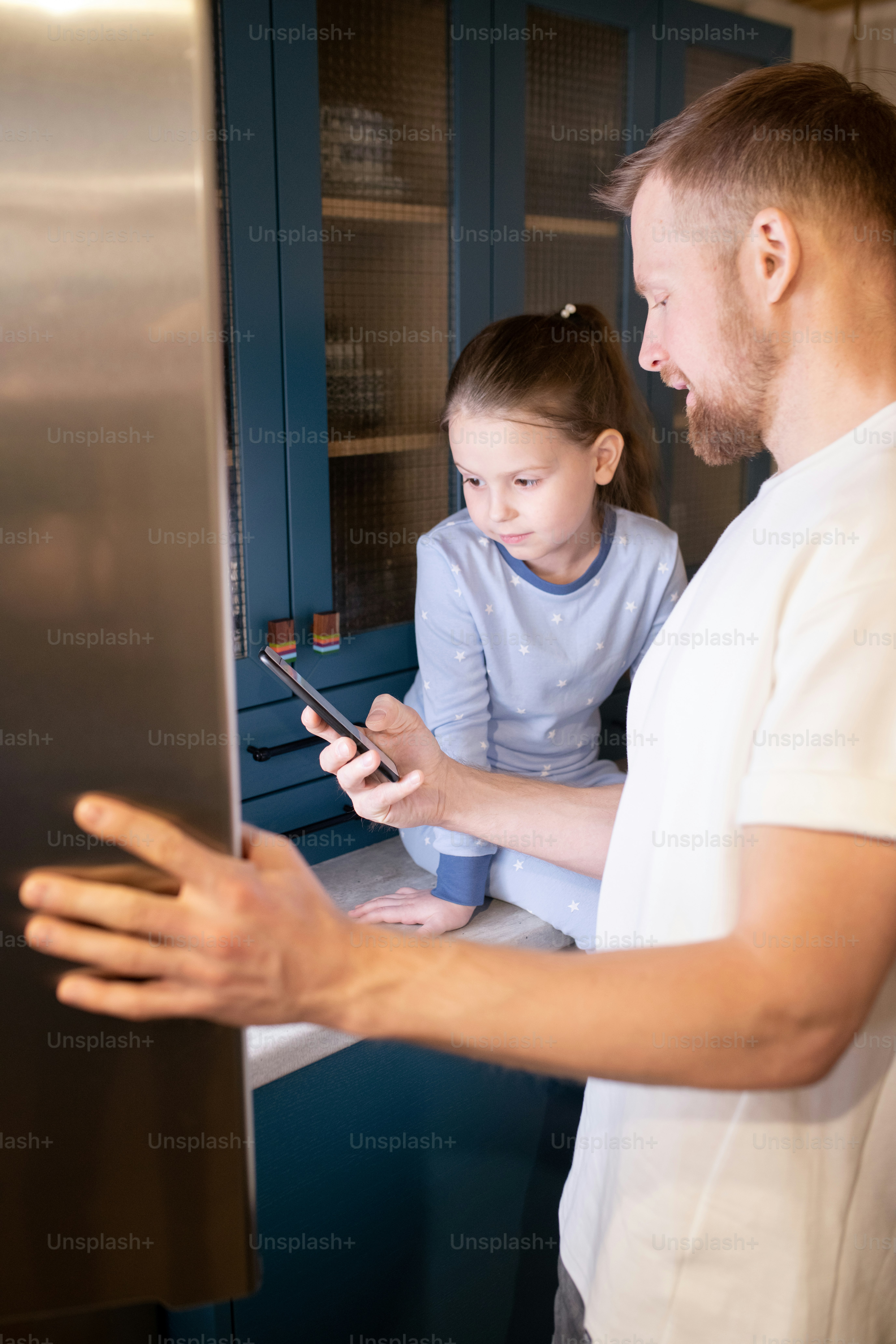 Young father showing his cute little daughter how to regulate temperature in refrigerator while spending time together at home