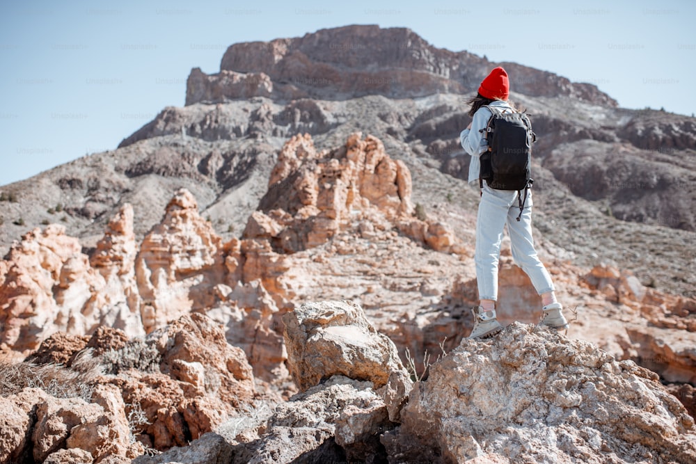 Giovane donna vestita casualmente in jeans con cappello rosso e zaino in spalla che cammina sul terreno roccioso in una giornata di sole. Viaggiando sulla valle vulcanica sull'isola di Tenerife