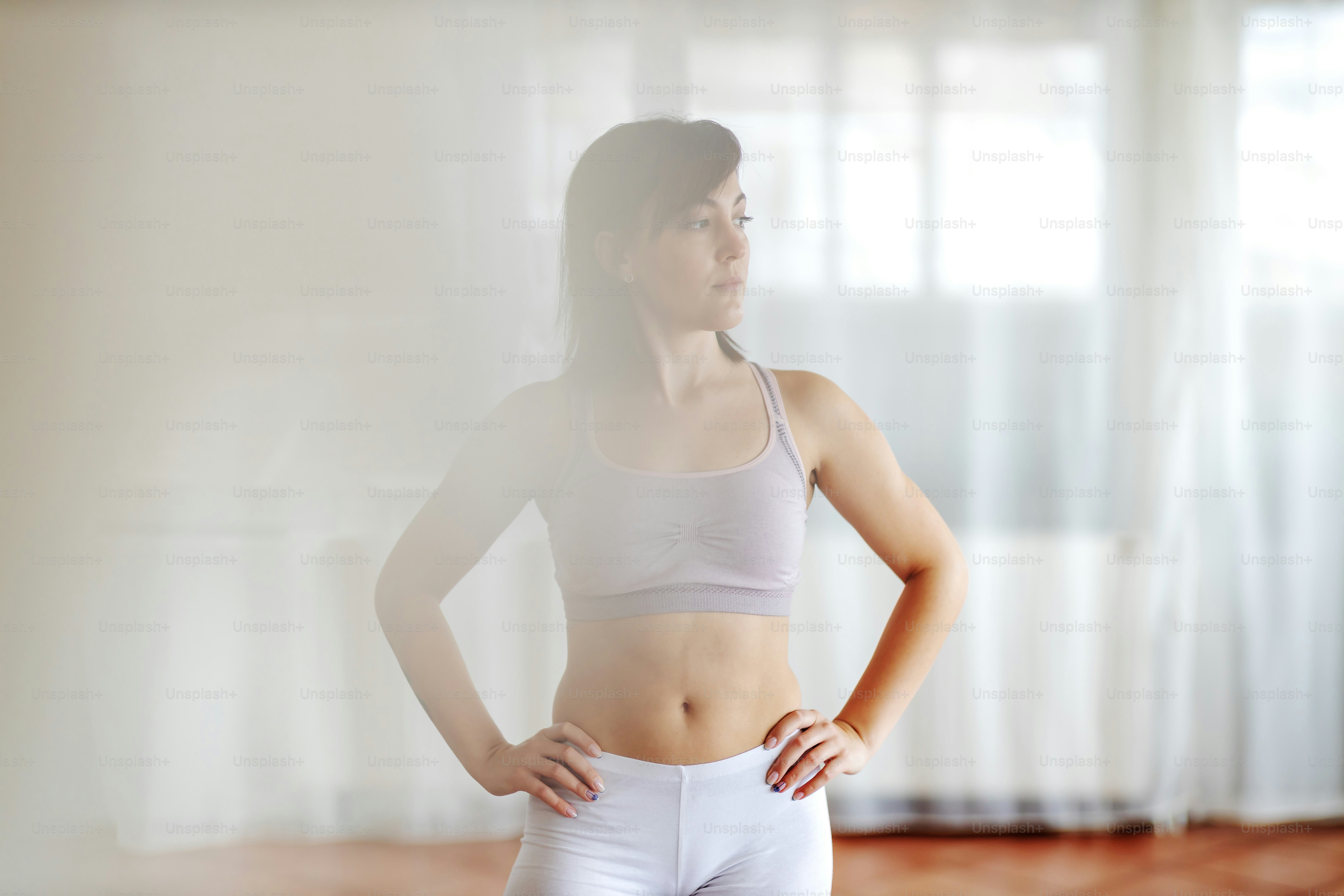 Junge attraktive Brünette steht mit den Händen in den Hüften und schaut weg.