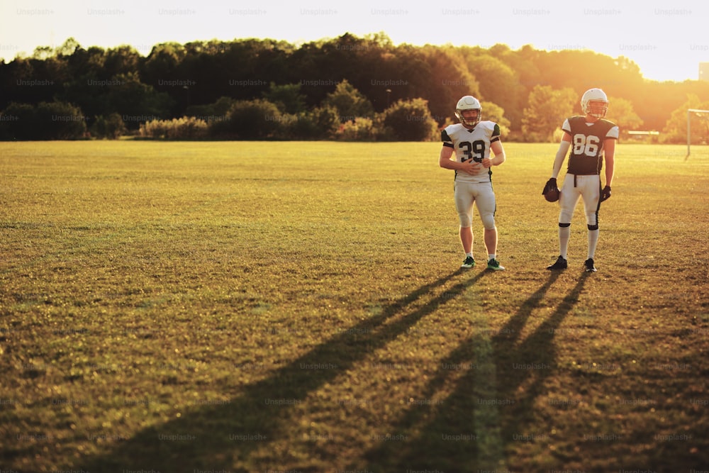 Two American football players standing together on a playing field during a lateafternoon team practice
