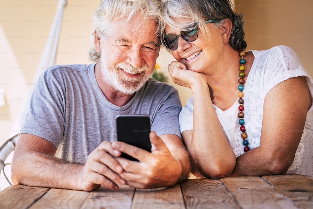 Happy beautiful senior old couple do a phone call with modern online technology device - retired cheeful people together forever with love and friendship - caucasian matures and internet connection