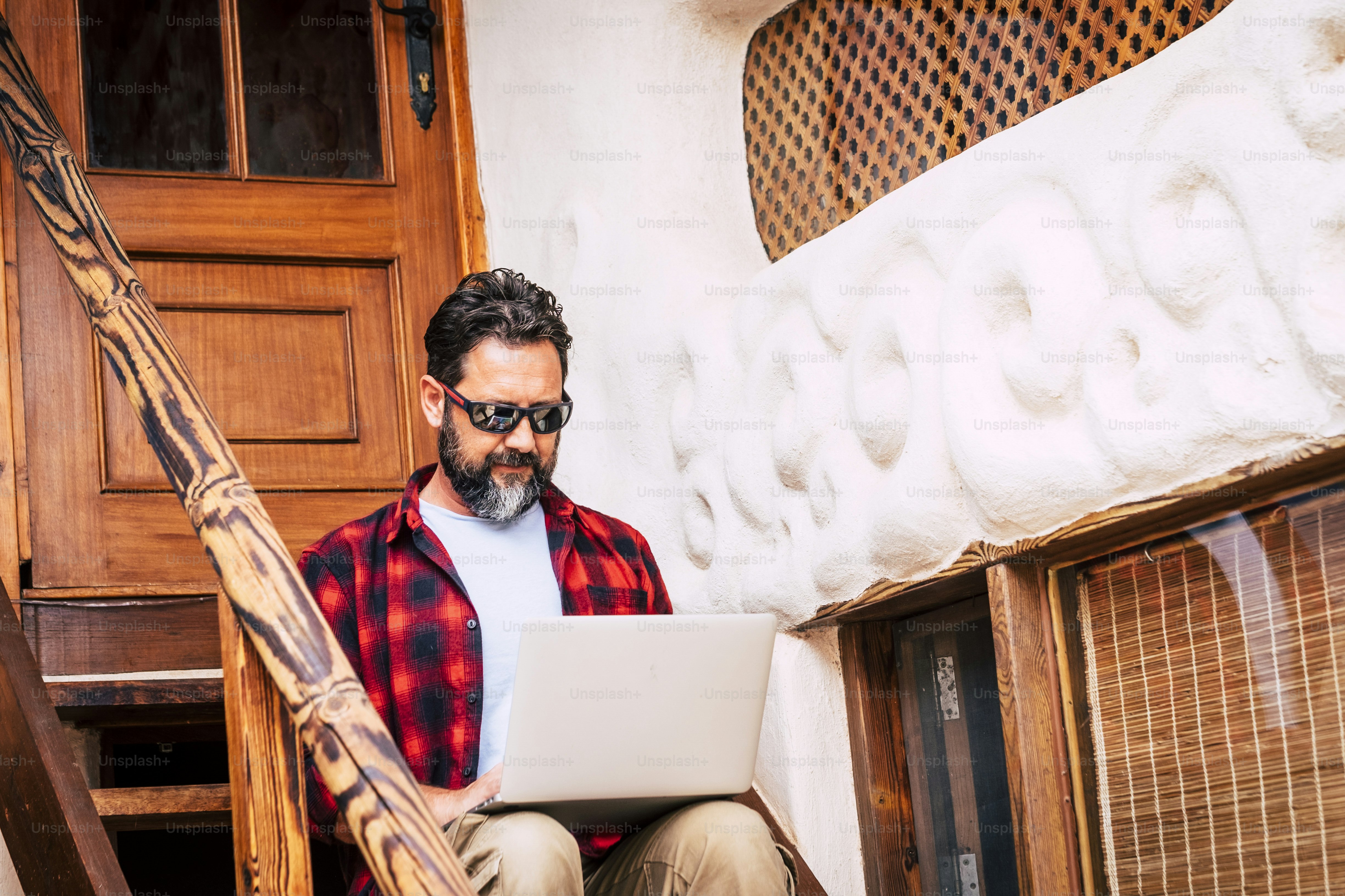 Caucasian adult man work with personal laptop computer sitting on the outdoor stairs at home - technology concept for modern job - internet connection and communicate people