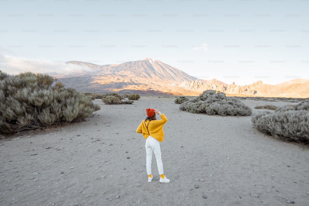 Stylish woman in bright clothes on the beautiful volcanic valley with volcano on the background during a sunset. Traveling on Tenerife island, Spain