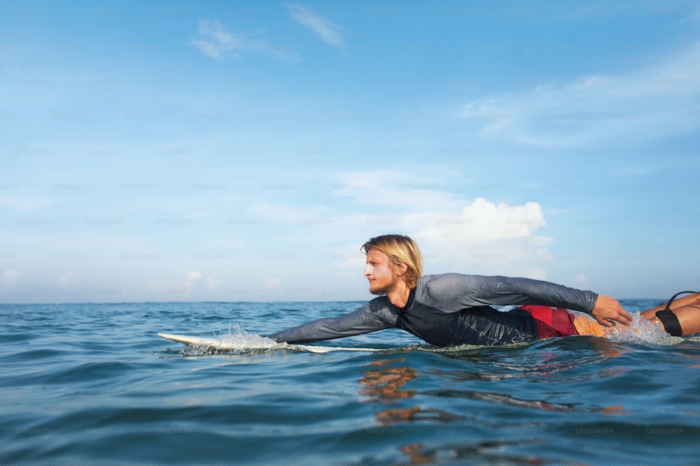 Surf. Surfista guapo en retrato de tabla de surf. Chico en traje de neopreno practicando en el océano. Deporte acuático para un estilo de vida activo.