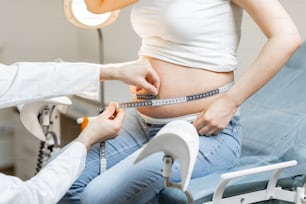 診察中に妊婦の腹部をテープで測定する医師、腹部に焦点を合わせた顔のないトリミングされたビュー