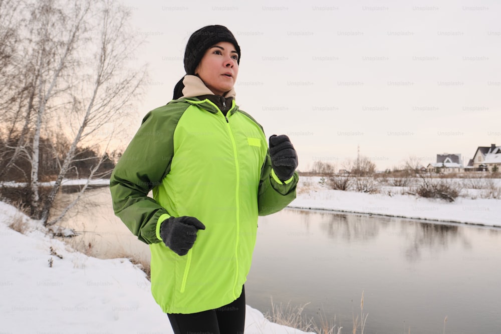 緑のジャケットと手袋で若い魅力的な女性は、冬の海岸に沿ってジョギング