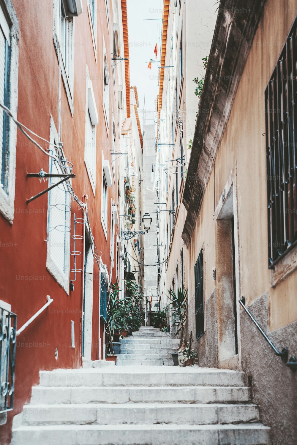 Uma vista vertical de grande angular de uma típica rua estreita portuguesa num bairro residencial de Lisboa, com casas de habitação em ambos os lados e escadas que se estendem até à distância; perspectiva decrescente