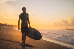Surfe. Surfista carregando prancha de surf na praia do oceano. Silhueta do homem no belo nascer do sol em Bali.