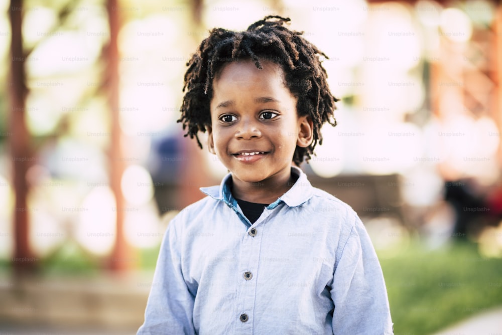 公園の屋外の焦点がぼけた背景に、黒人のアフリカ人の子供のポートレート – 色と肌の人種の多様性の子供のコンセプトと、陽気な子供が微笑んで幸せになる – 代替ドレッドヘア