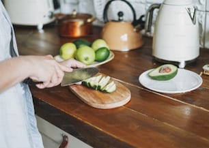 Female hands cut avocado on wooden working surface in kitchen at home