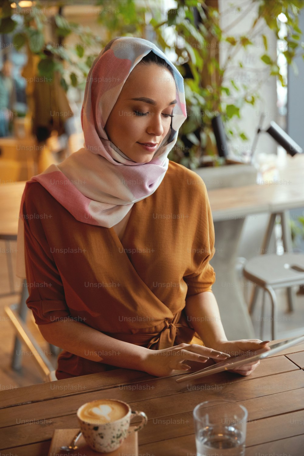 Menina em Hijab. Retrato bonito da mulher muçulmana. Mulher sentada no café e trabalhando no tablet. Modelo olhando para a tela e leitura.