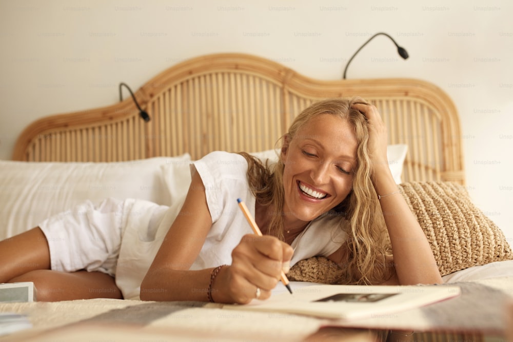 Trabaja desde casa. La mujer madura usa el bloc de notas sentado en la cama. Retrato de belleza de una mujer de mediana edad estudiando y trabajando. Concepto de lugar de trabajo cómodo.