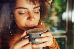 Closeup of mixed race woman holding cup of coffee and smelling it.