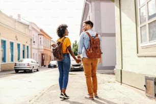 Rear view of attractive cute hipster multicultural couple walking on the street on rainy day.