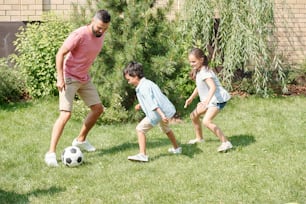 裏庭の芝生で息子と娘とサッカーをする現代の父親