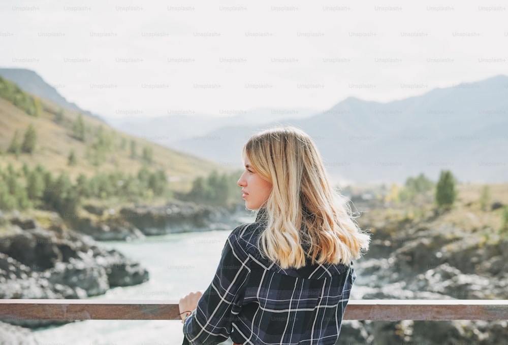 Junge blonde Frau in Kleidung auf der Horochowski-Brücke am Fluss Katun, Altai-Gebirge