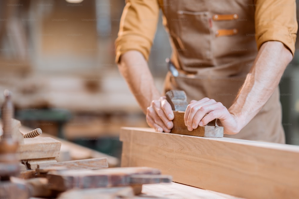 Carpinteiro trabalhando com uma madeira, aplainando uma barra com um avião na oficina de carpintaria. Close-up nas mãos