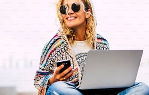 Portrait of cheerful adult caucasian woman working outdoor with phone and laptop computer in roaming technology - free from office lifestyle modern people concept