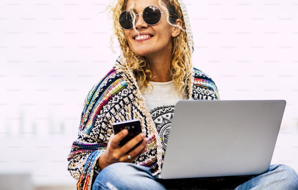 Portrait of cheerful adult caucasian woman working outdoor with phone and laptop computer in roaming technology - free from office lifestyle modern people concept