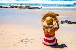 Tourist woman and tourism lifestlye in summer holiday vacation at the beach in a sunny day and sun designed on the sand - blue water ocean in background and relax concept