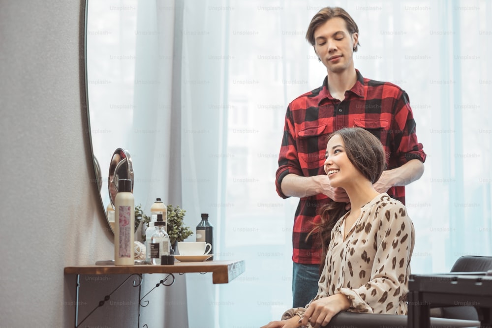 Barbero estilista peinando cabello largo para hermosa joven asiática en salón de belleza, momento de trabajo