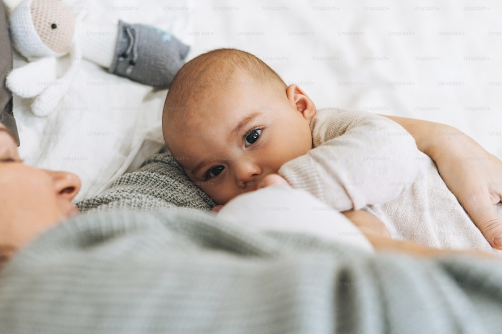 Young mom with cute baby boy, mother breast feeds baby on bed, natural tones