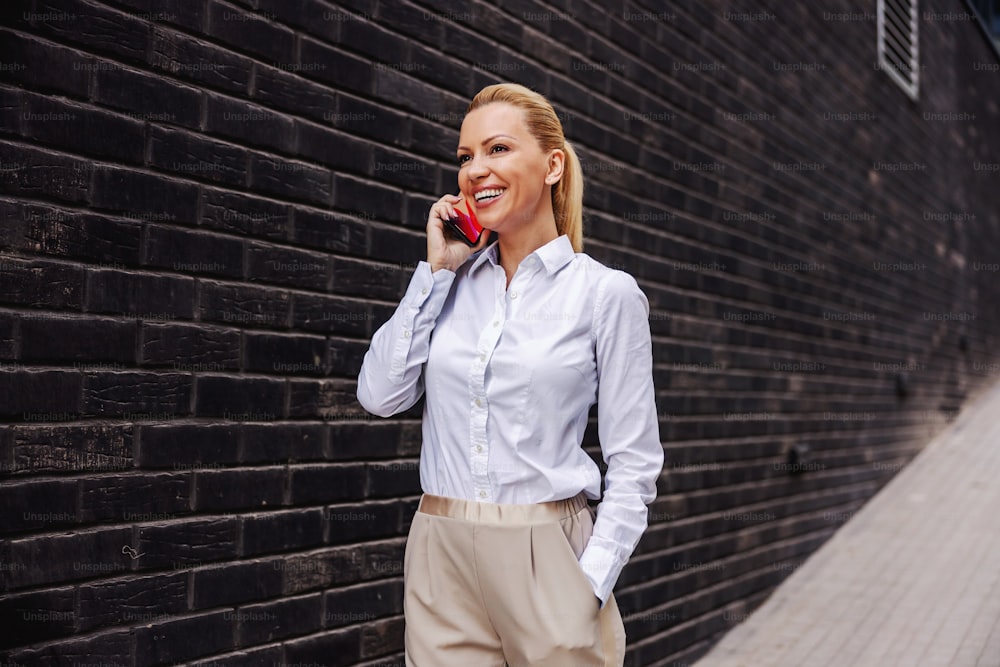 Attractive smiling fashionable woman walking outdoors and talking on the phone.