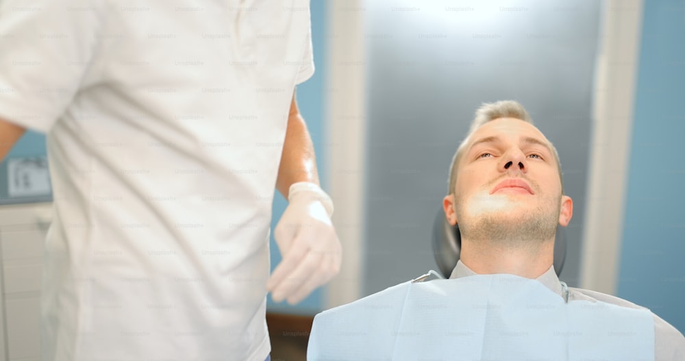 Male patient waiting for the dentist, sitting on a dental chair preparing for the dental treatment. Dentist coming wearing gloves. 4k video screenshot, please use in small size