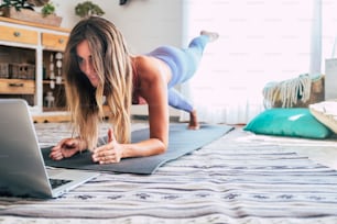운동복을 입은 스포티한 여성이 거실에서 집에서 노트북 컴퓨터를 사용하여 바닥에 자세를 취하고 있습니다. 스포츠 및 레크리에이션 개념과 건강한 라이프 스타일 실내