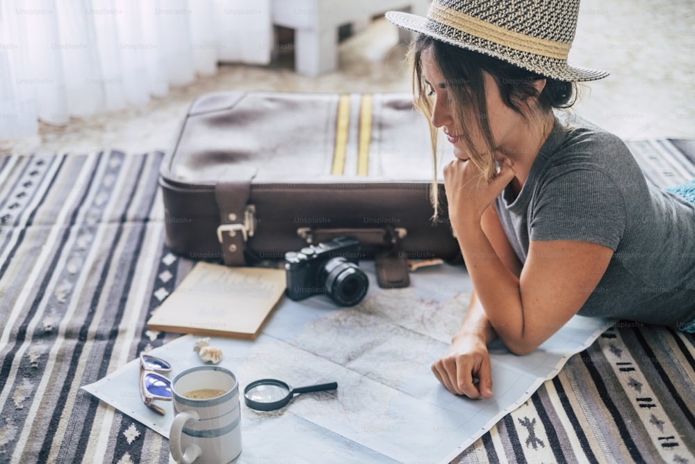 Caucasian woman planning vacation travel with map and guide at home, female people plan next holidays vacation while relaxing on the floor - pretty girl wanderlust concept