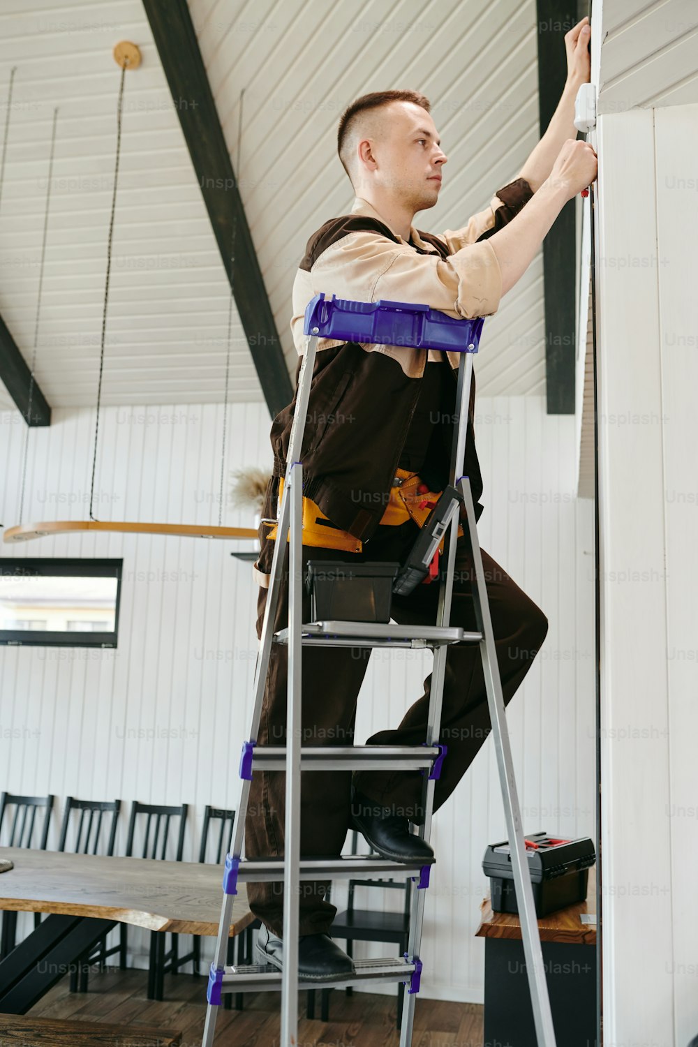 Young repairman in uniform climbing a ladder while doing his work