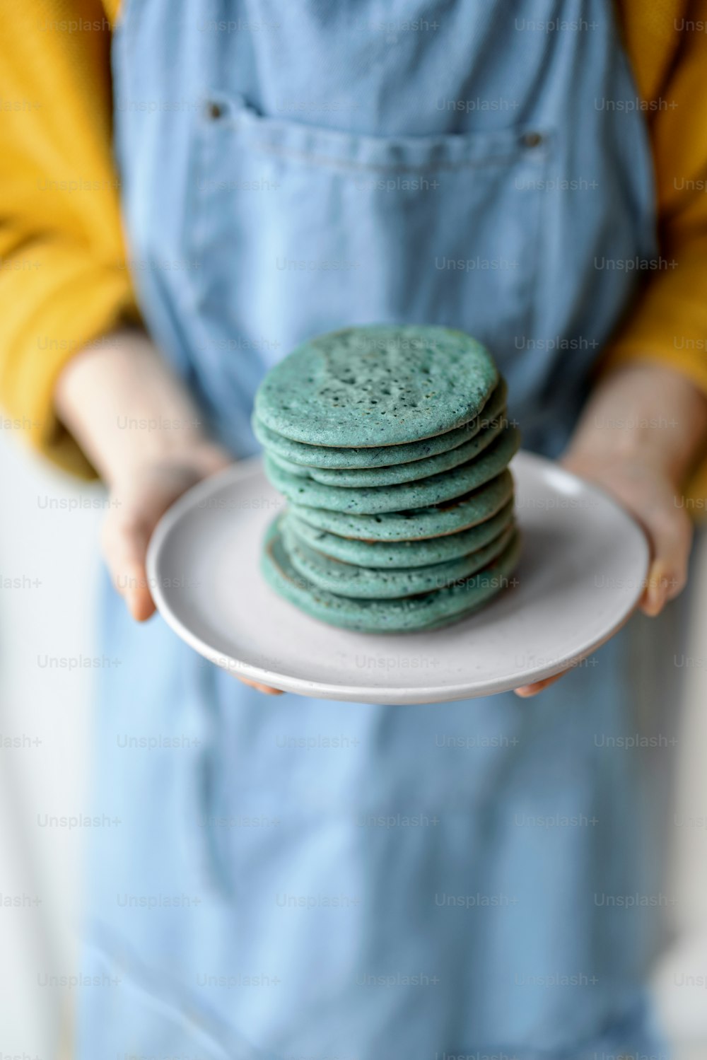 Woman in blue apron holding a stack of blue pancakes on a plate. Homemade delicious breakfast.