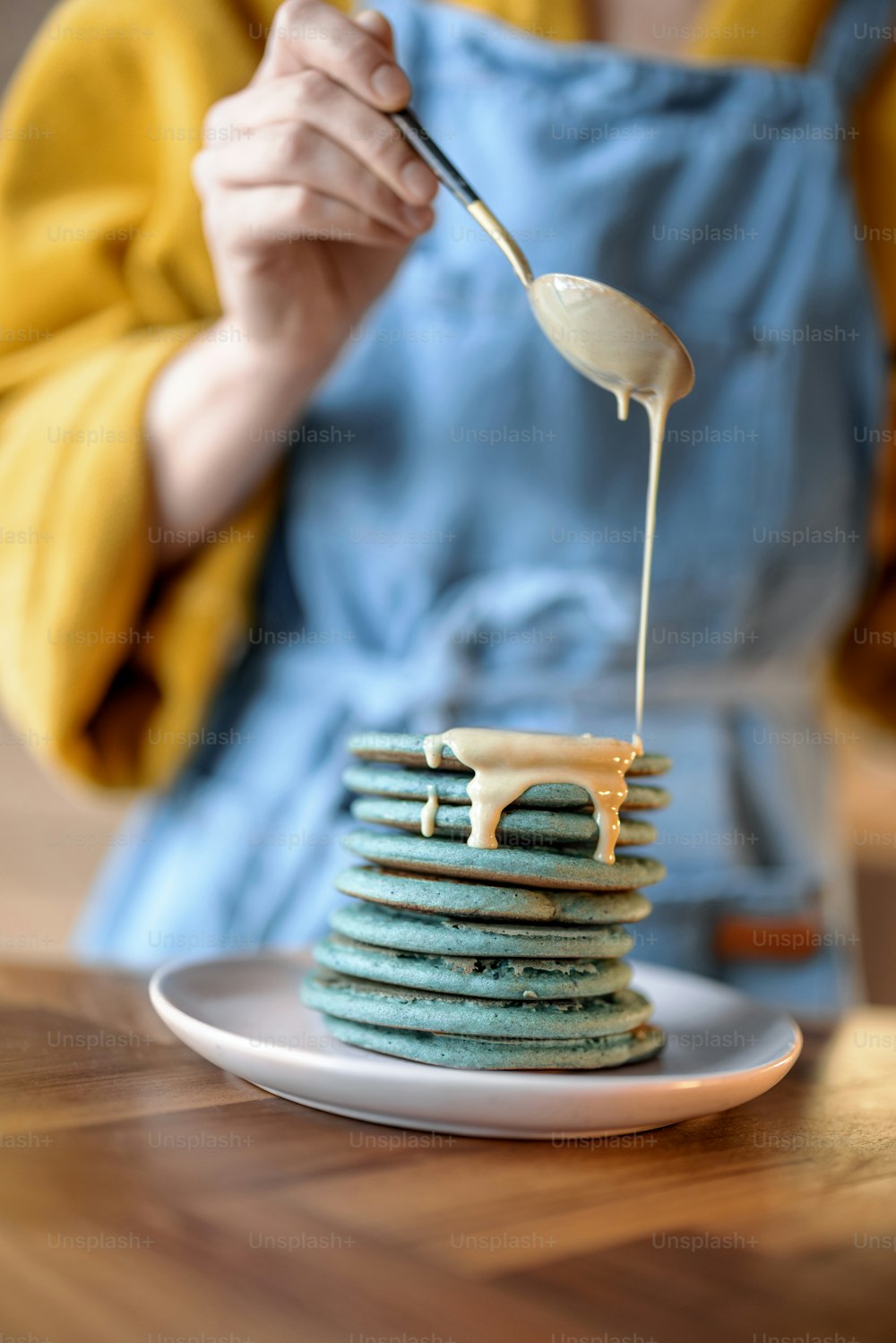 Mulher no avental azul derramando panquecas azuis com souse de caramelo na mesa de madeira. Comida caseira saborosa. Celebração de Shrovetide.