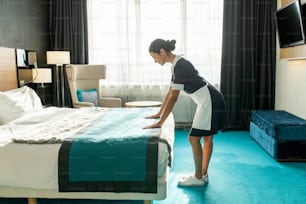 Bonita camarera inclinada sobre la cama hecha en la habitación del hotel