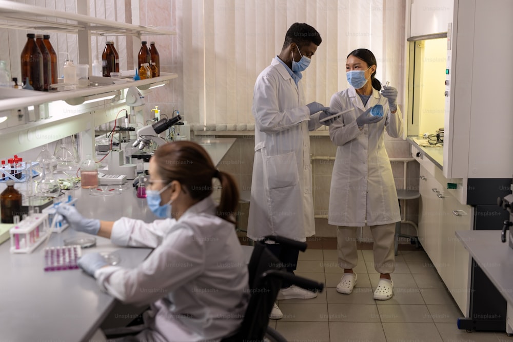 Intercultural chemists in labcoats working with new liquid substances together