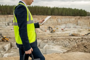 Contemporary architect in uniform using tablet while moving along construction site