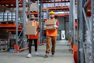 Dos cargadoras en ropa de trabajo que transportan cajas con mercancías