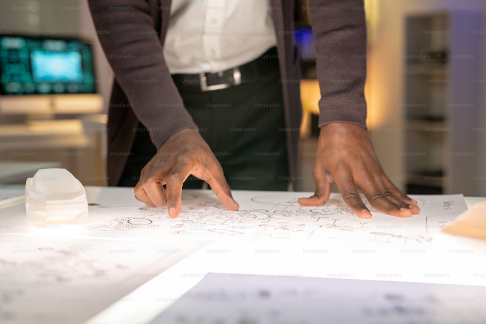 Close-up of unrecognizable black designer standing at desk and examining car sketch in office